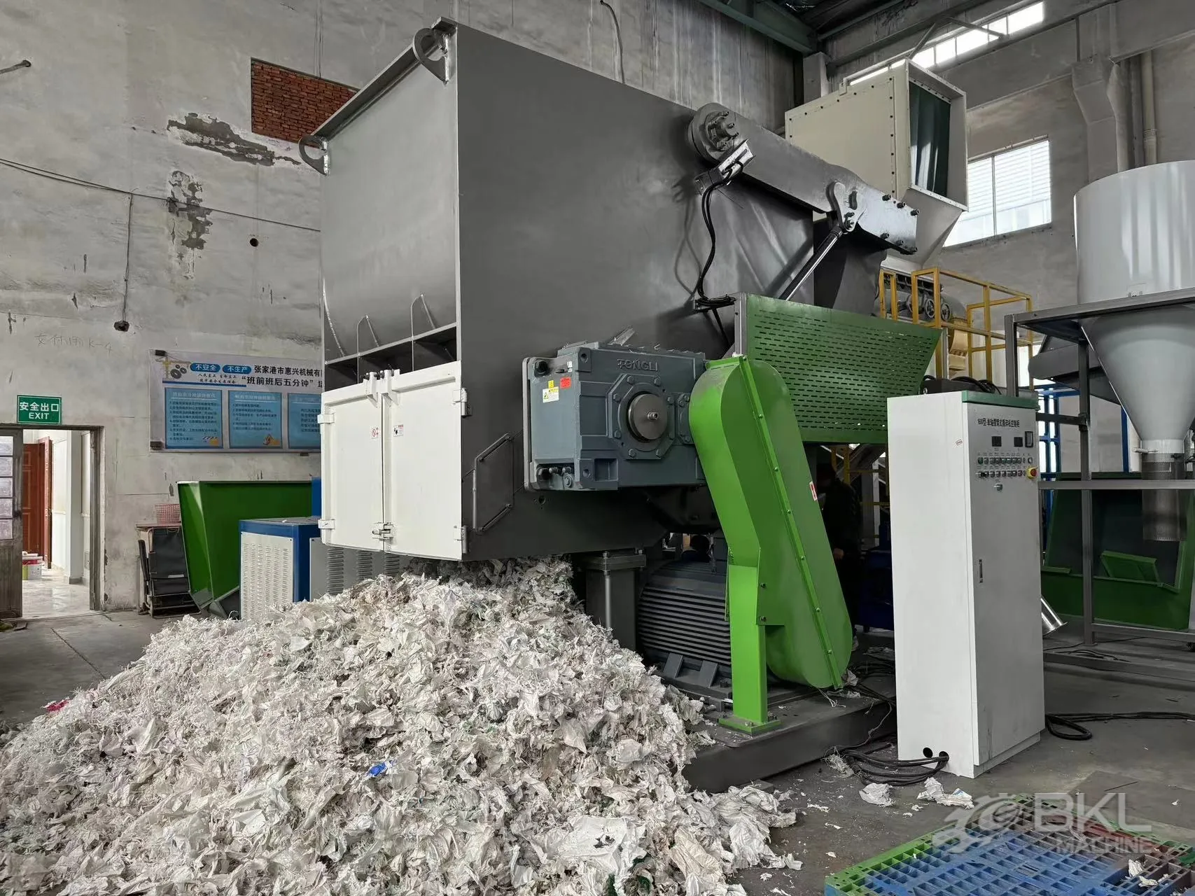 Single-shaft shredder in operation with a pile of shredded white film flakes and a control cabinet