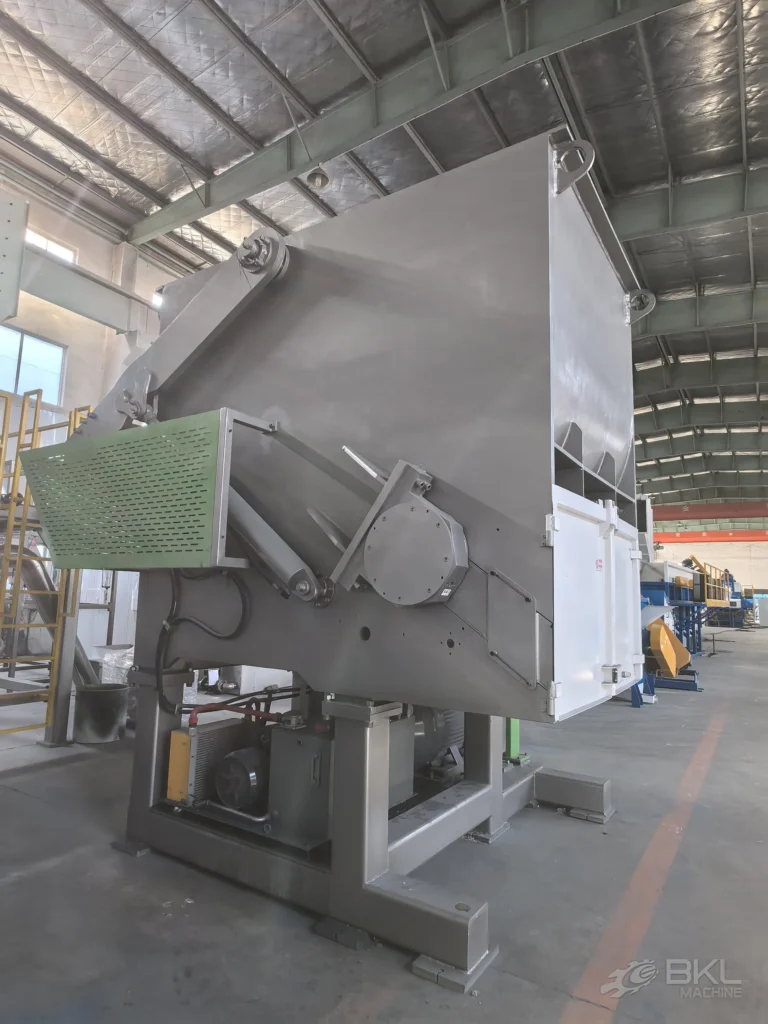 Large single-shaft shredder from the side showing the swing-arm hopper and hydraulic power pack below