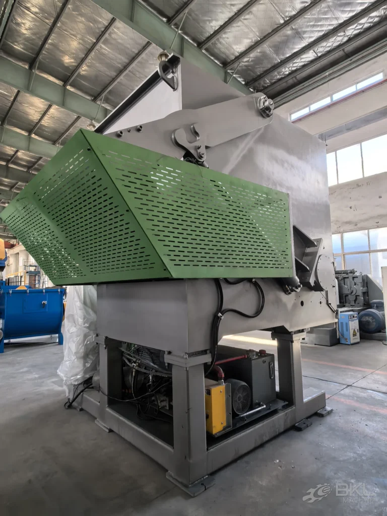 Shredder drive end with a large perforated green belt guard and yellow hydraulic pump unit underneath