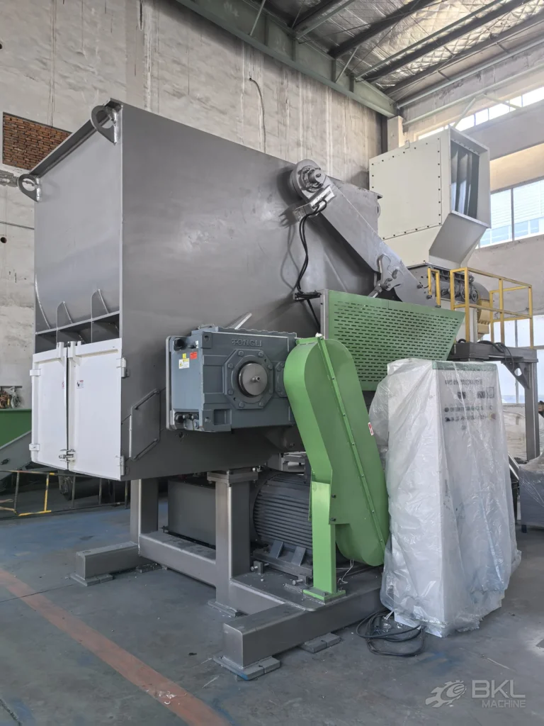 Single-shaft shredder with gearbox, green belt guard and main motor seen from the discharge side