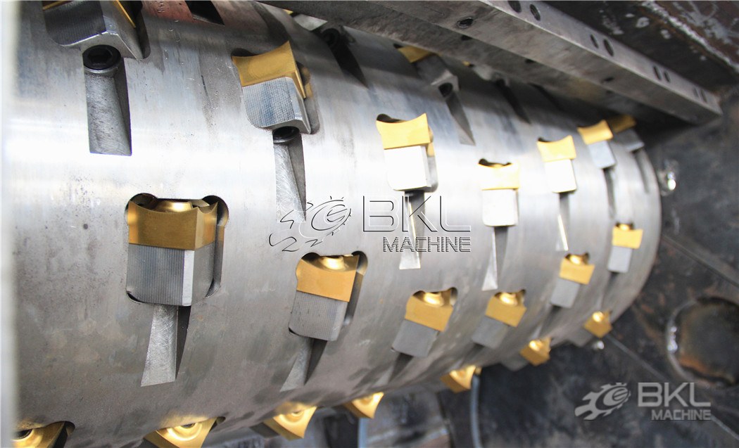 Solid drum rotor with golden square carbide inserts bolted in a helical pattern beside the counter knife