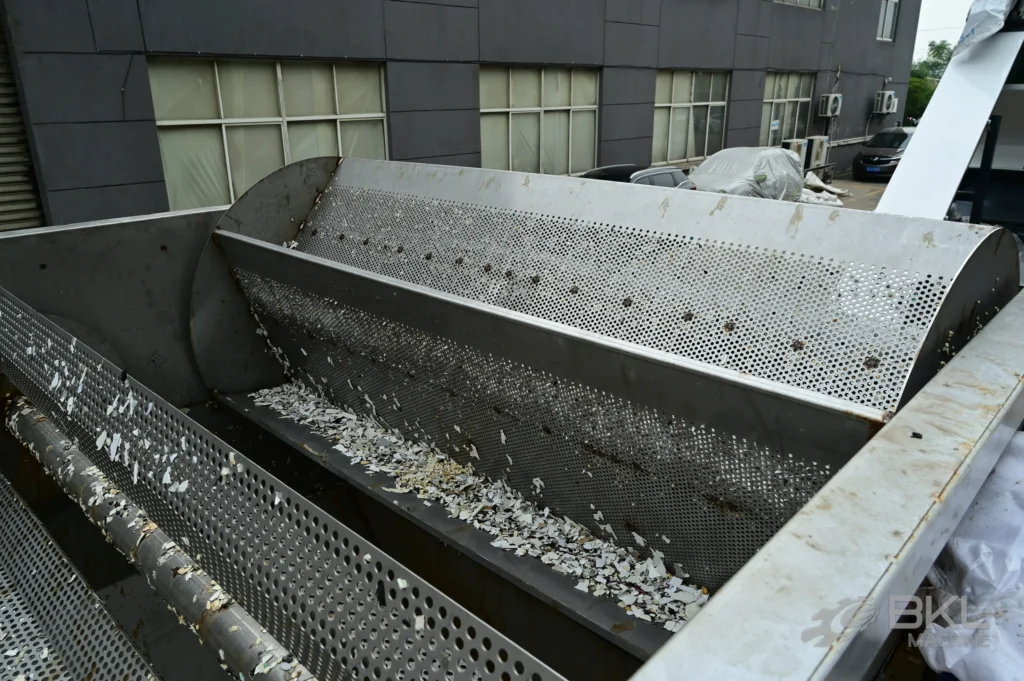 Perforated stainless washing trough with discharge screw holding white rigid plastic flakes after rinsing