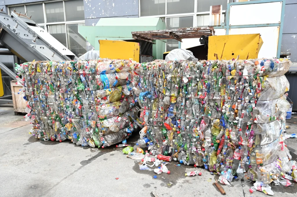 Baled post-consumer PET bottles stacked outdoors beside the infeed conveyor of a washing line