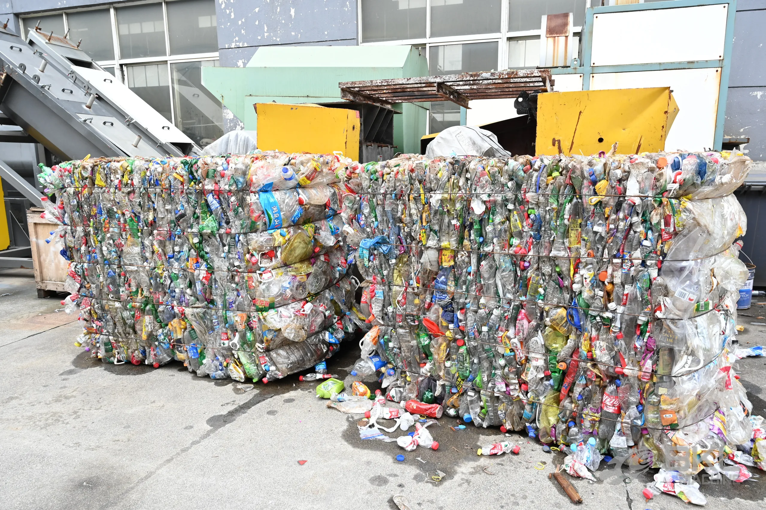 Baled post-consumer PET bottles stacked outdoors beside the infeed conveyor of a washing line