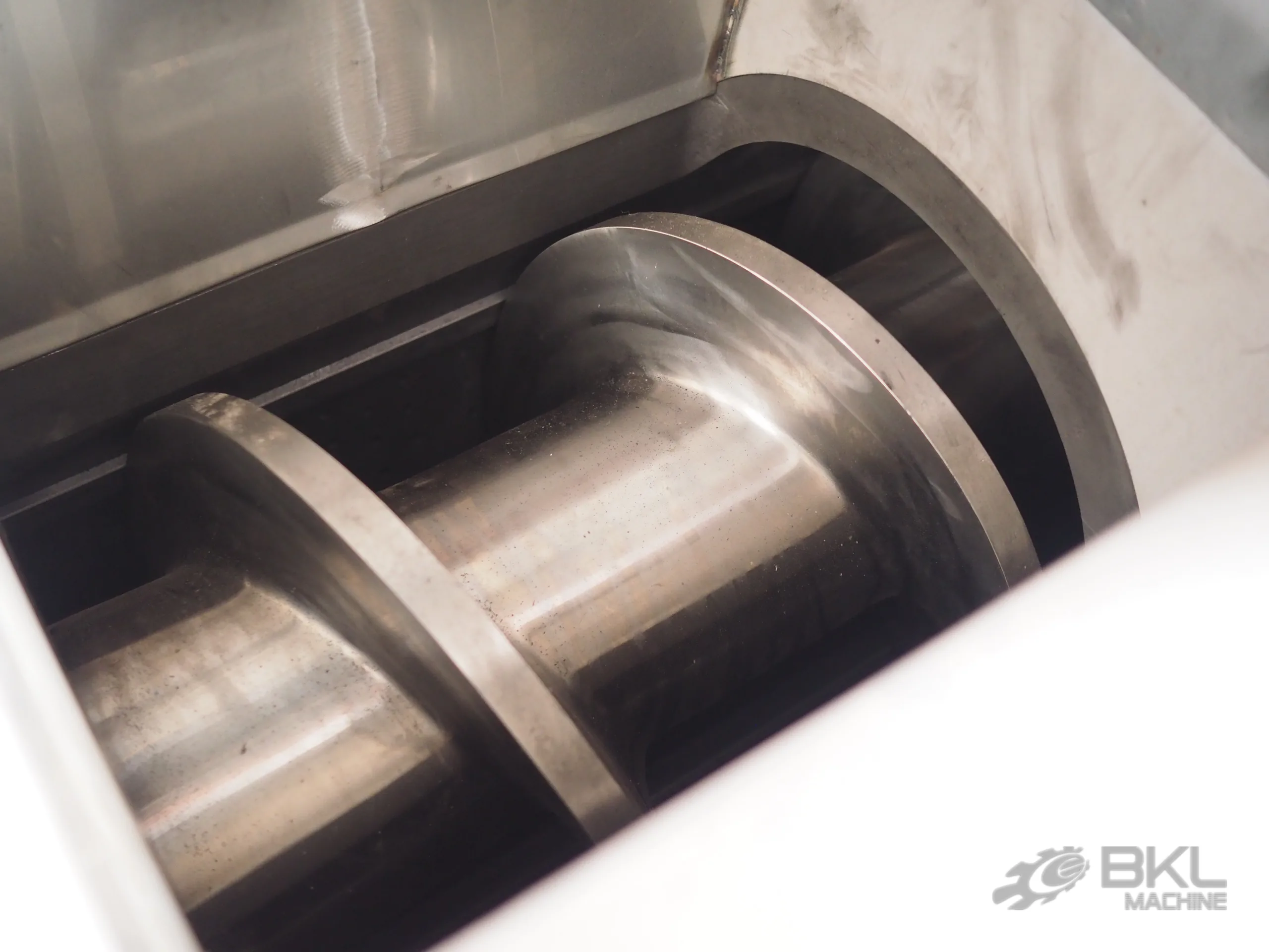 Close-up into the squeezer feed throat showing the polished compression screw flights inside the barrel
