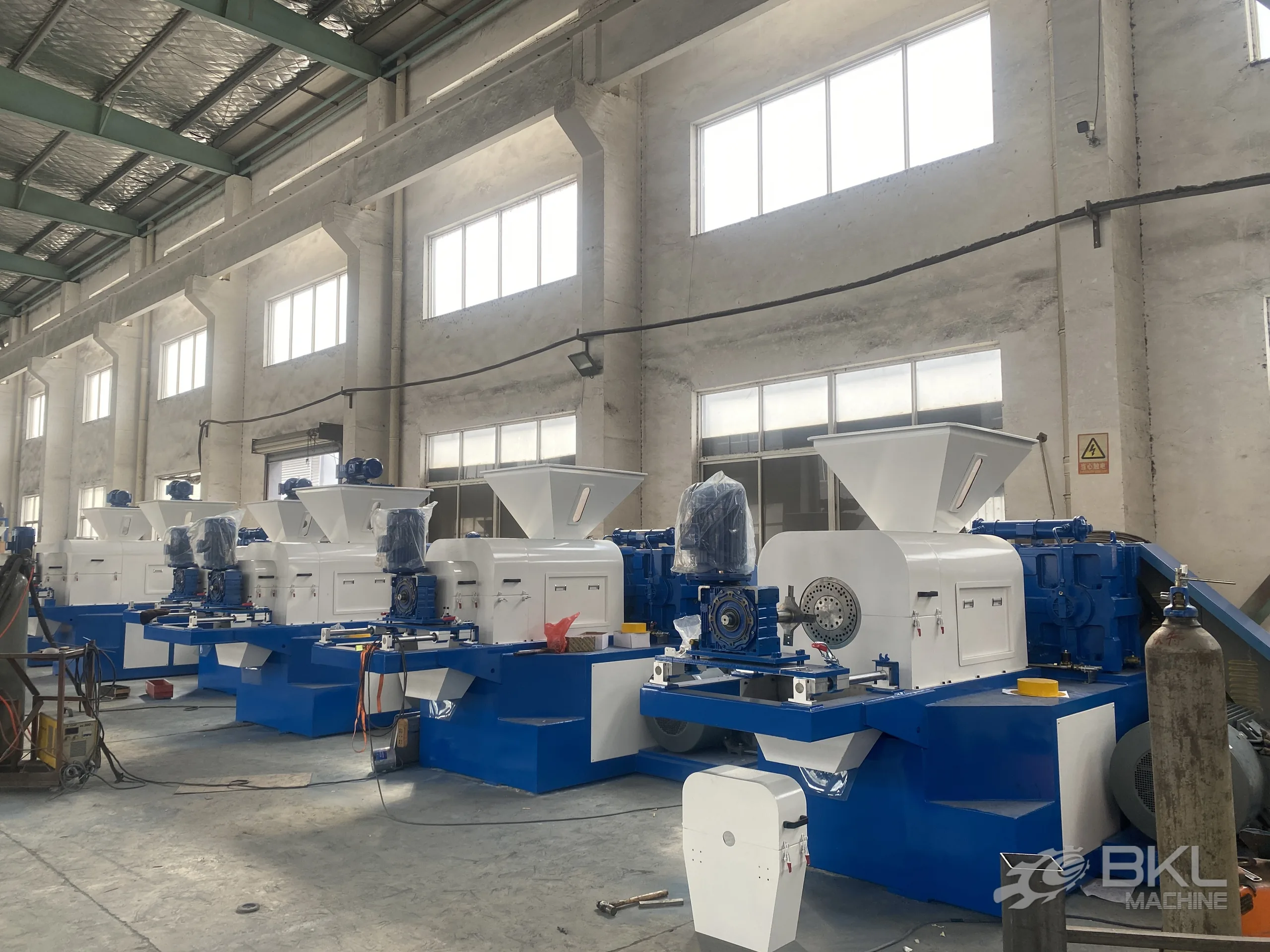 Squeezer units under assembly with the perforated die plate and blue gearbox exposed on the nearest machine