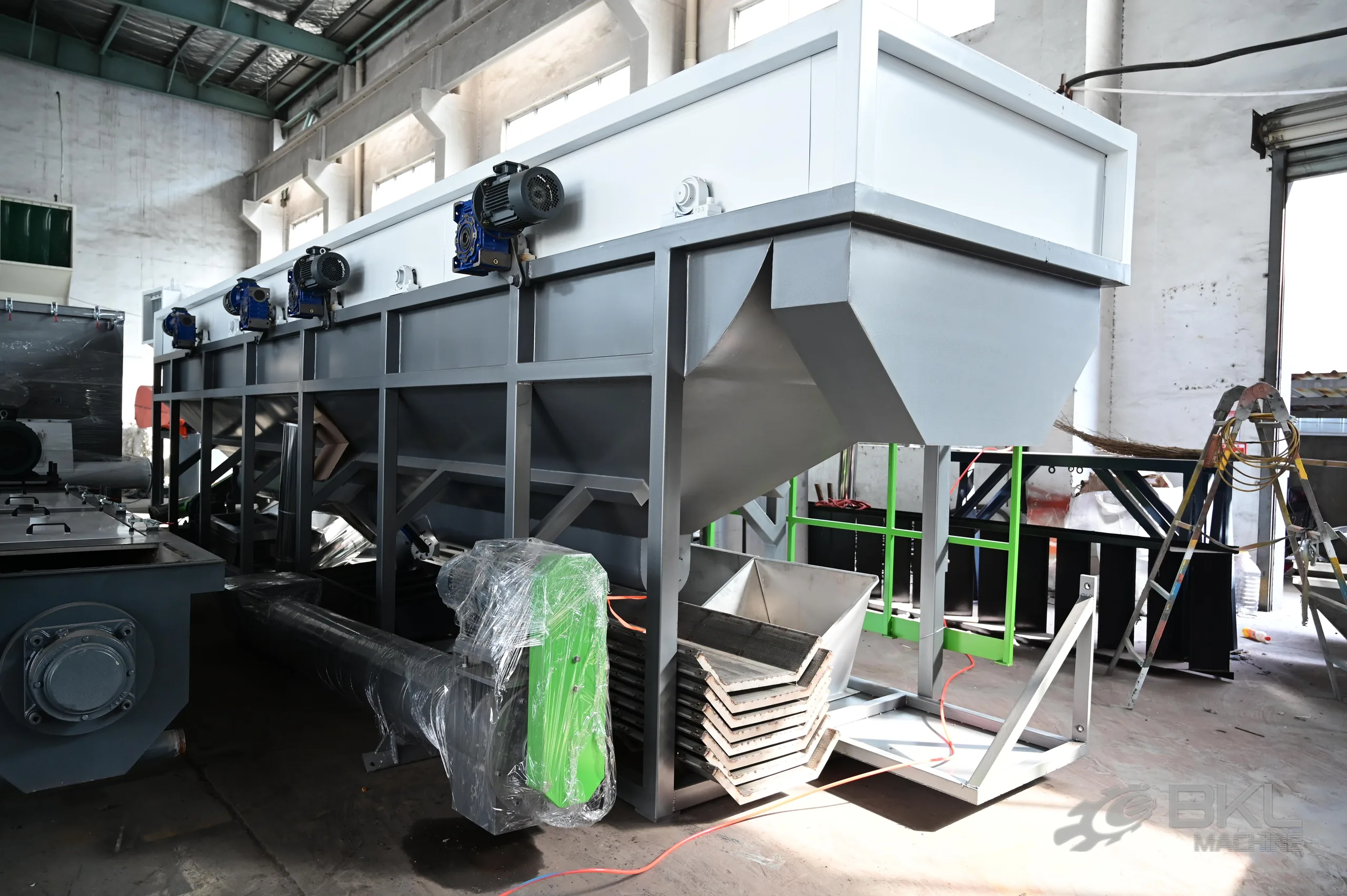 Sink-float tank under assembly with a row of blue paddle gearmotors, hopper bottoms and stacked cover panels