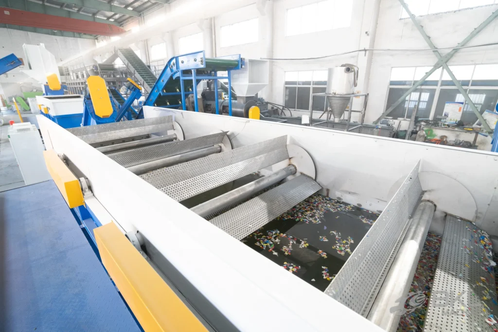 Looking into a working sink-float tank with coloured plastic flakes floating between perforated paddle rollers