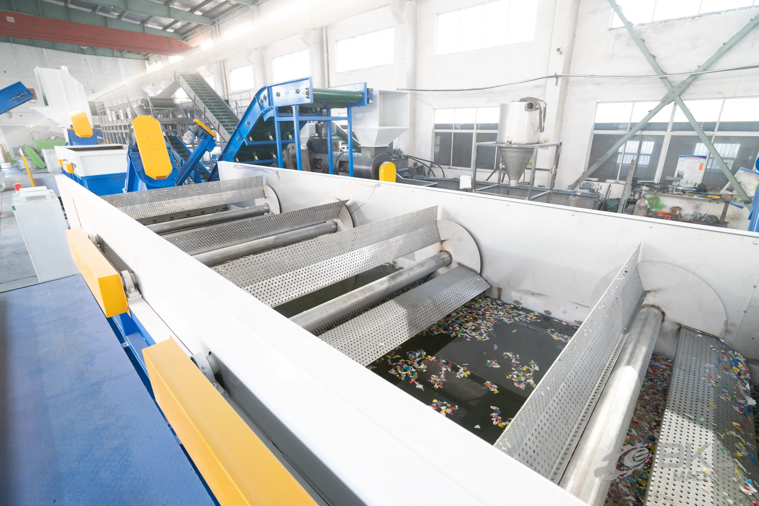 Looking into a working sink-float tank with coloured plastic flakes floating between perforated paddle rollers