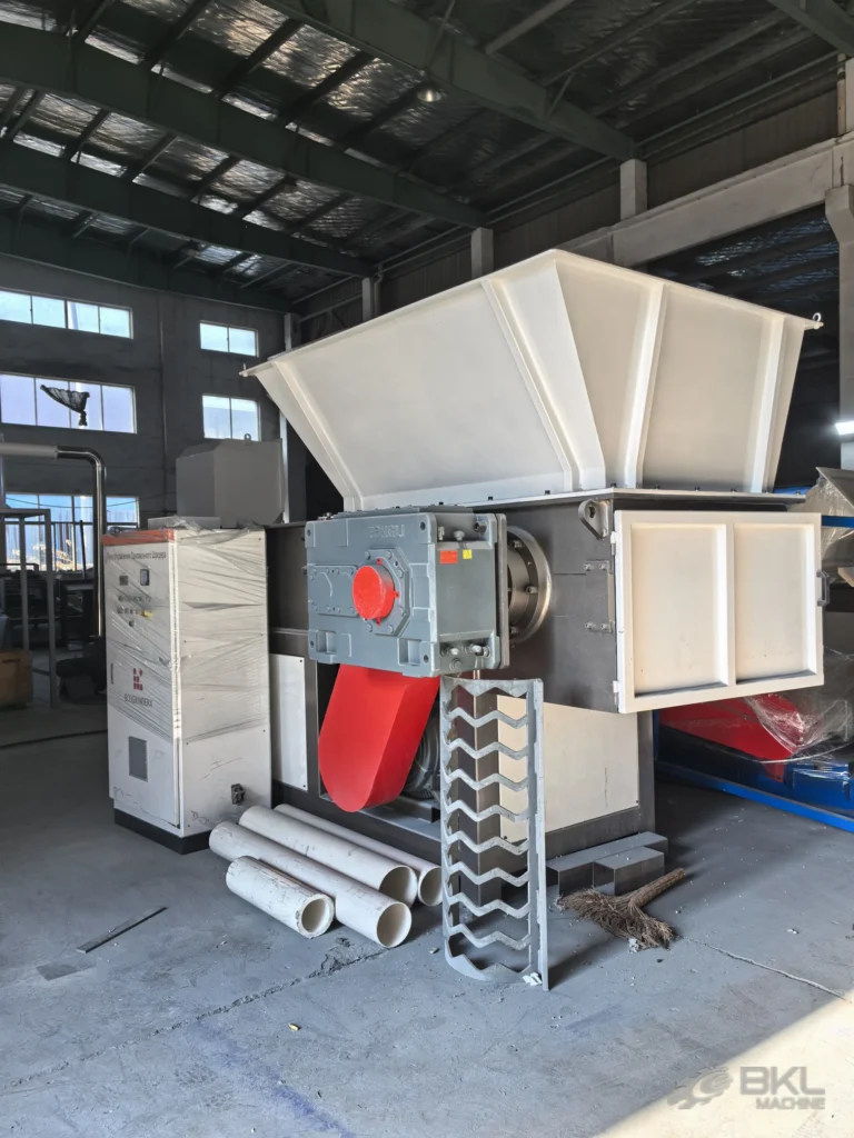 Large SS1000 single-shaft shredder with wide feed hopper and red belt guard beside white PVC pipe offcuts
