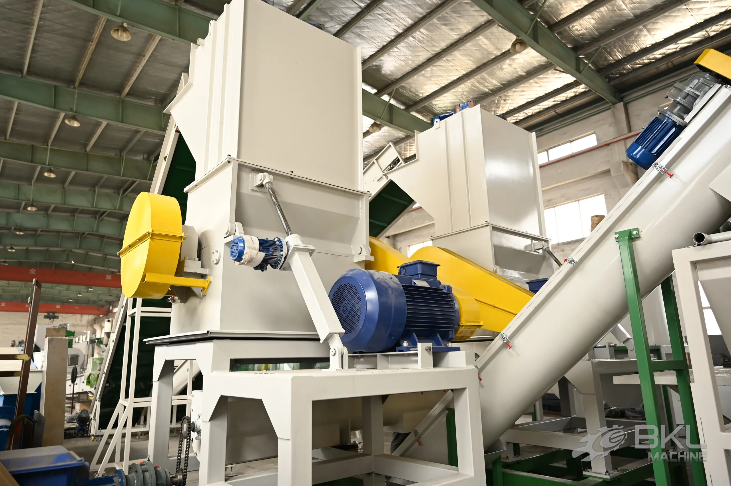 Two plastic crushers with blue drive motors and inclined screw conveyors in a recycling line workshop