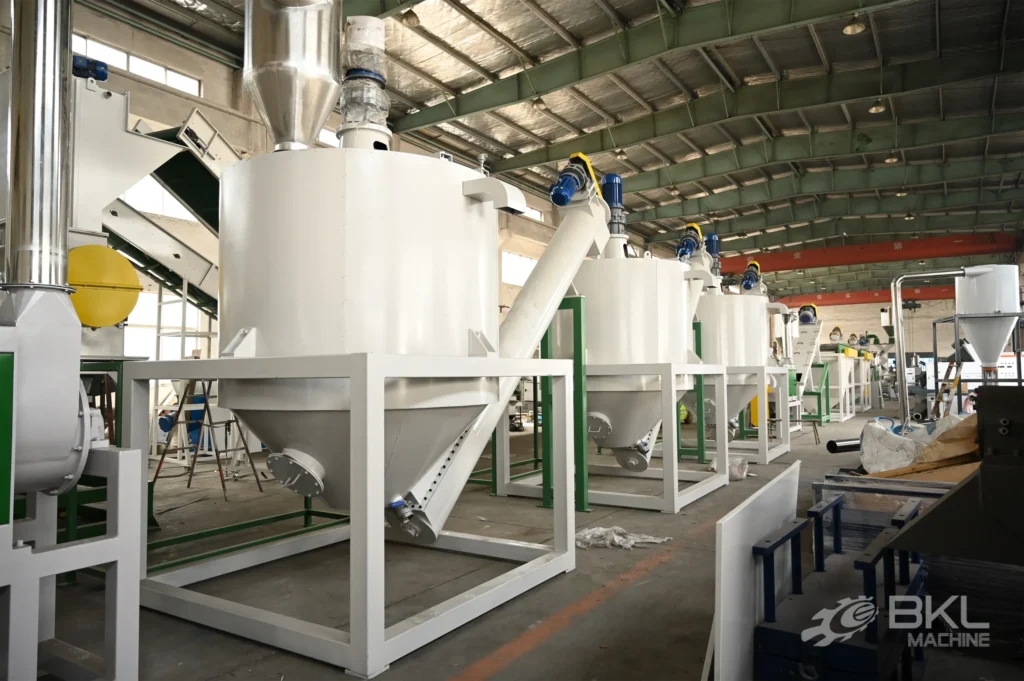 Row of conical silos with top agitators linked by screw conveyors at the end of a PET washing line