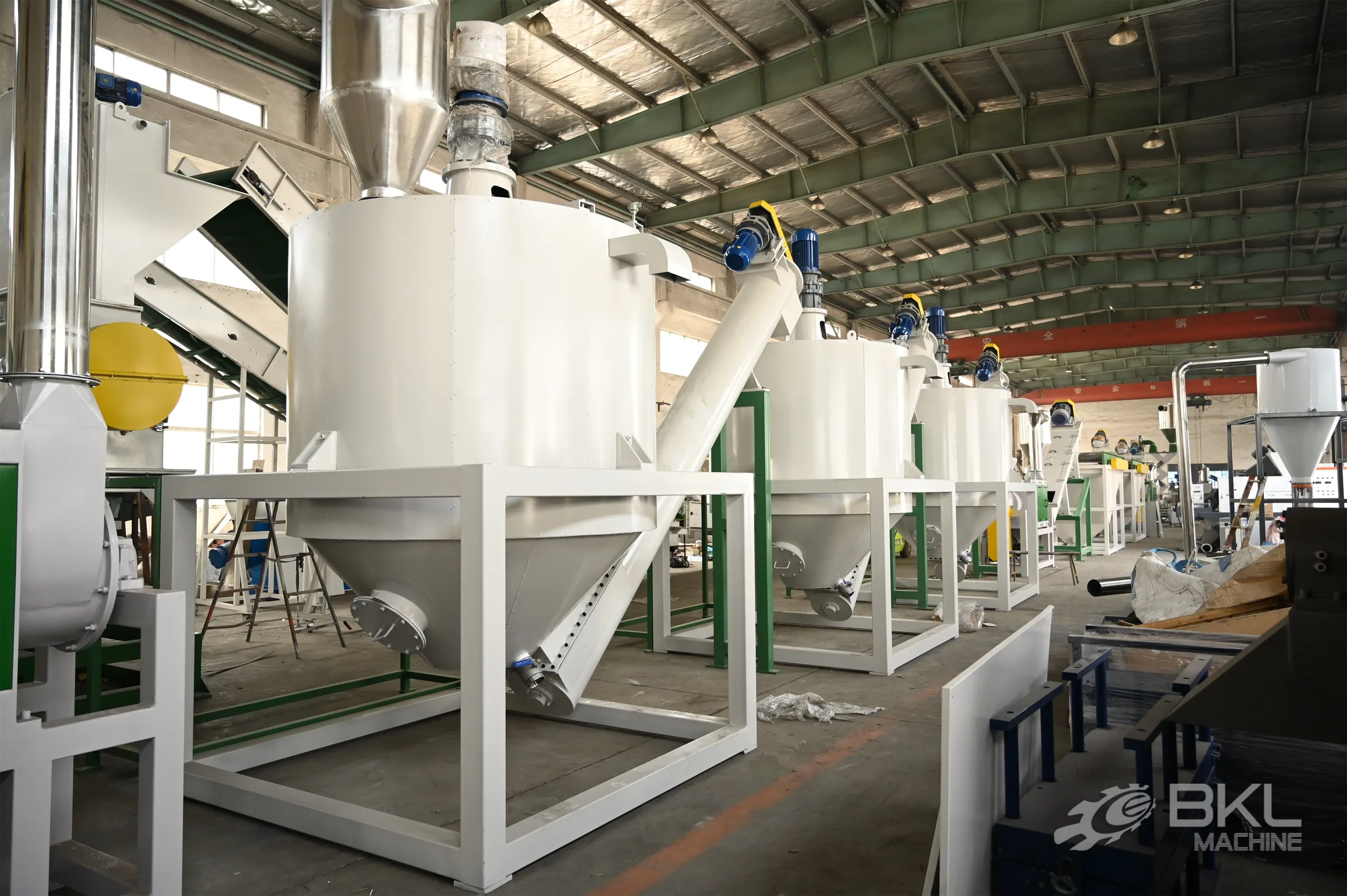 Row of conical silos with top agitators linked by screw conveyors at the end of a PET washing line