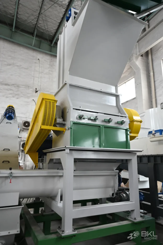 Plastic crusher installed in a washing line workshop with yellow belt guards above a screw conveyor