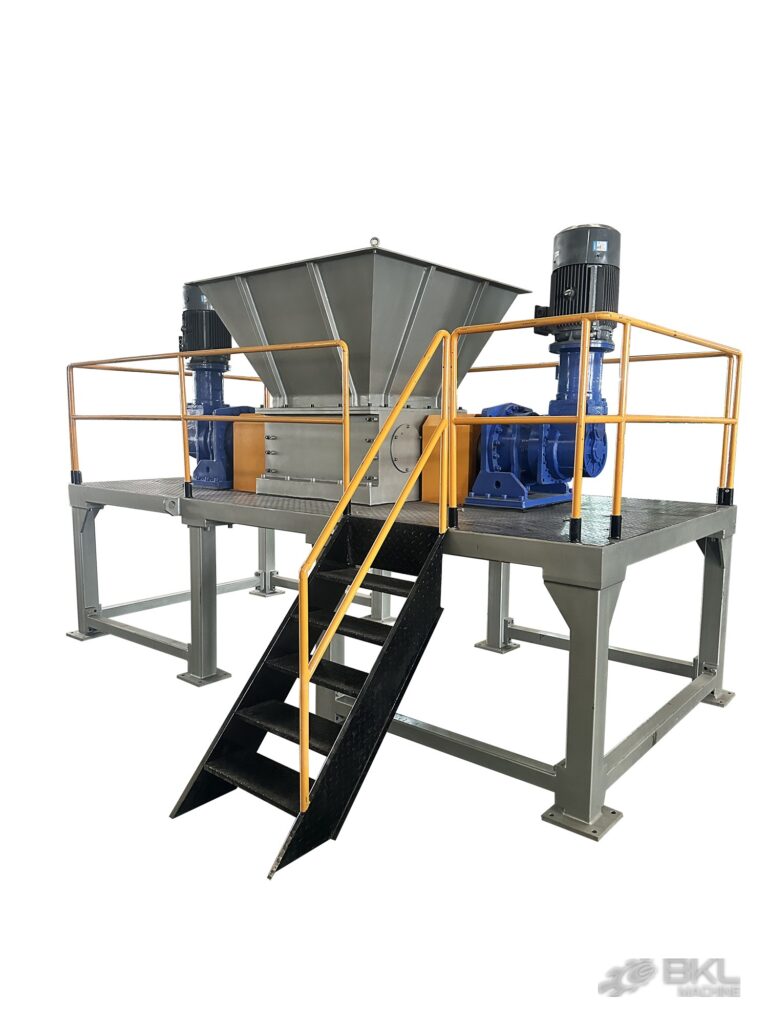 Twin-shaft shredder on a raised maintenance platform with yellow railings, access stair and two vertical motors