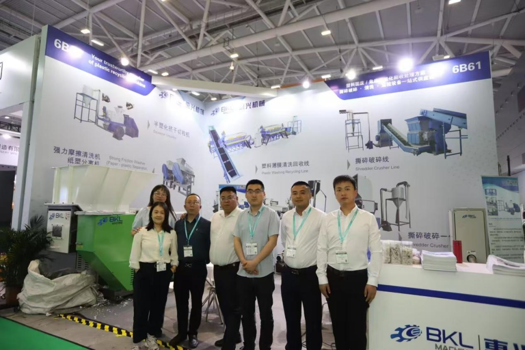 Sales and technical team at Booth 6B61 in front of the recycling line wall graphics at BKL-MACHINE