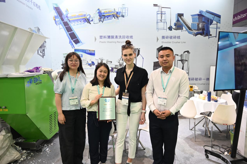 Staff and an overseas visitor holding a framed plaque at Booth 6B61 at BKL-MACHINE