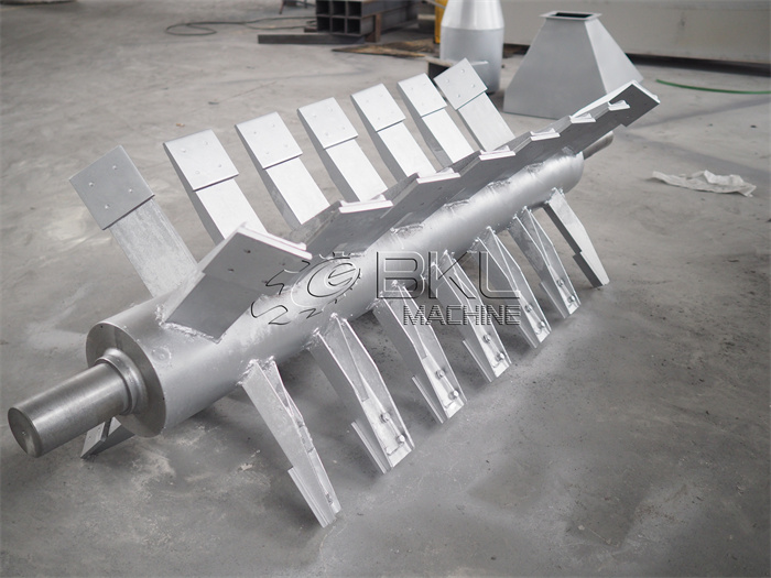 Centrifugal dryer rotor shaft laid on the floor, showing the row of angled vanes welded along its length.