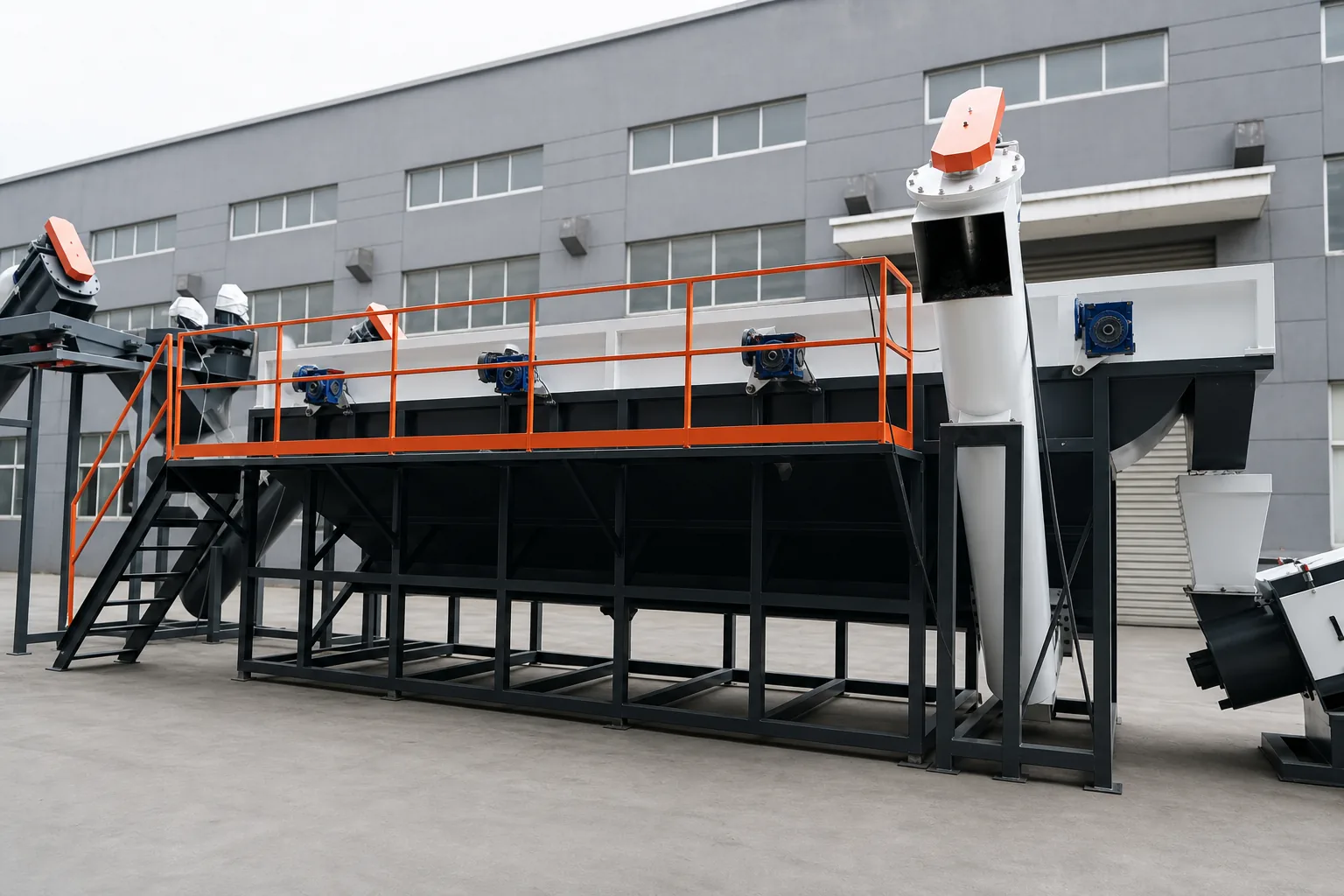 Long sink-float separation tank on a black steel frame with an orange walkway handrail, agitator gear motors along the rim and an inclined screw discharge conveyor at the far end