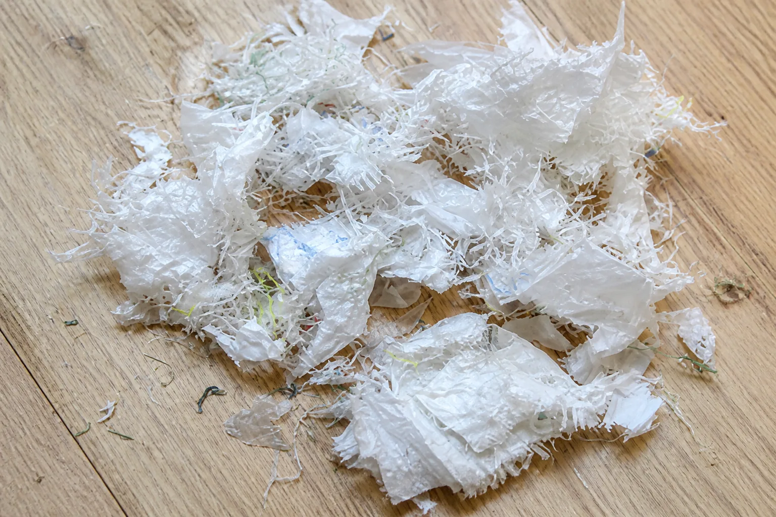Cleaned film shreds spread across a light timber bench top, mostly milky white with a few faint green and blue tinted pieces.