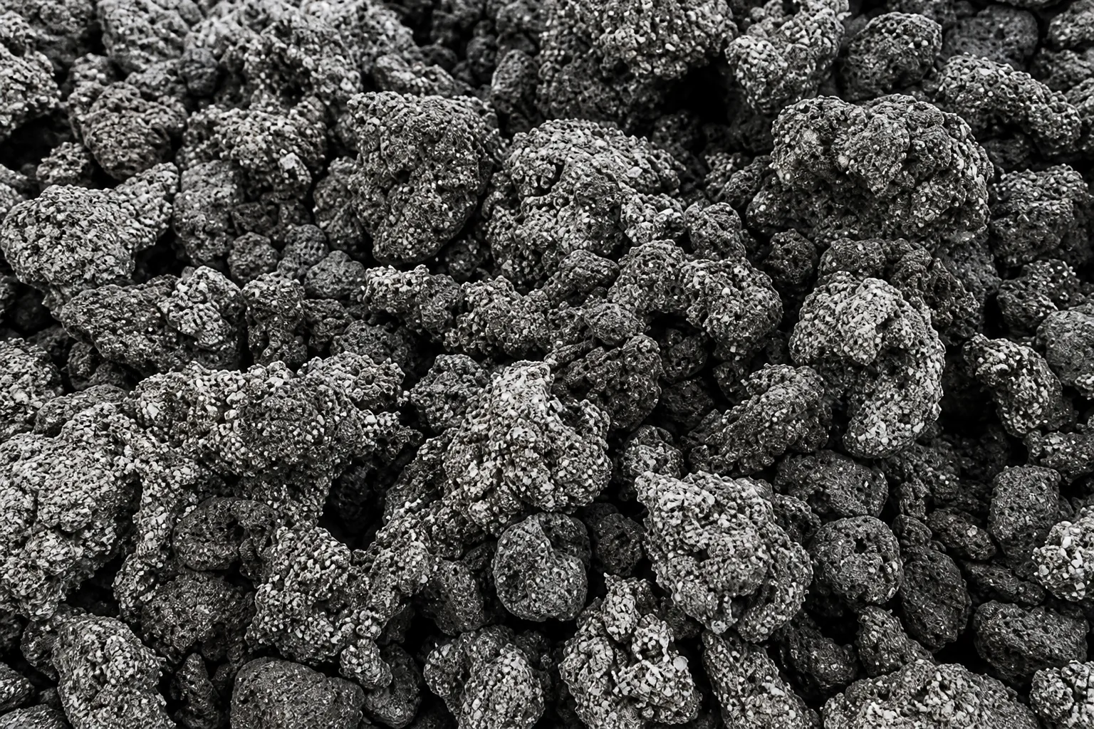 Pile of dark charcoal plastic agglomerate lumps with rough, pitted and speckled surfaces.