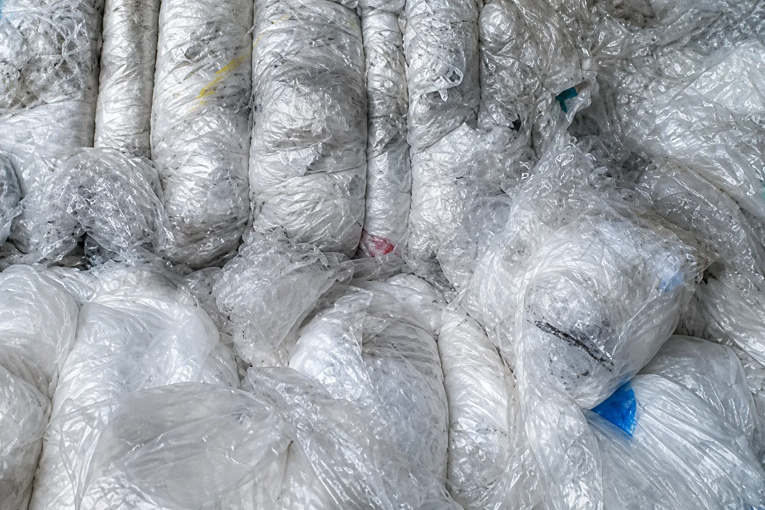 Close-up of compressed translucent LDPE film bags pressed into vertical folds, with a few blue and dark plastic fragments mixed in.