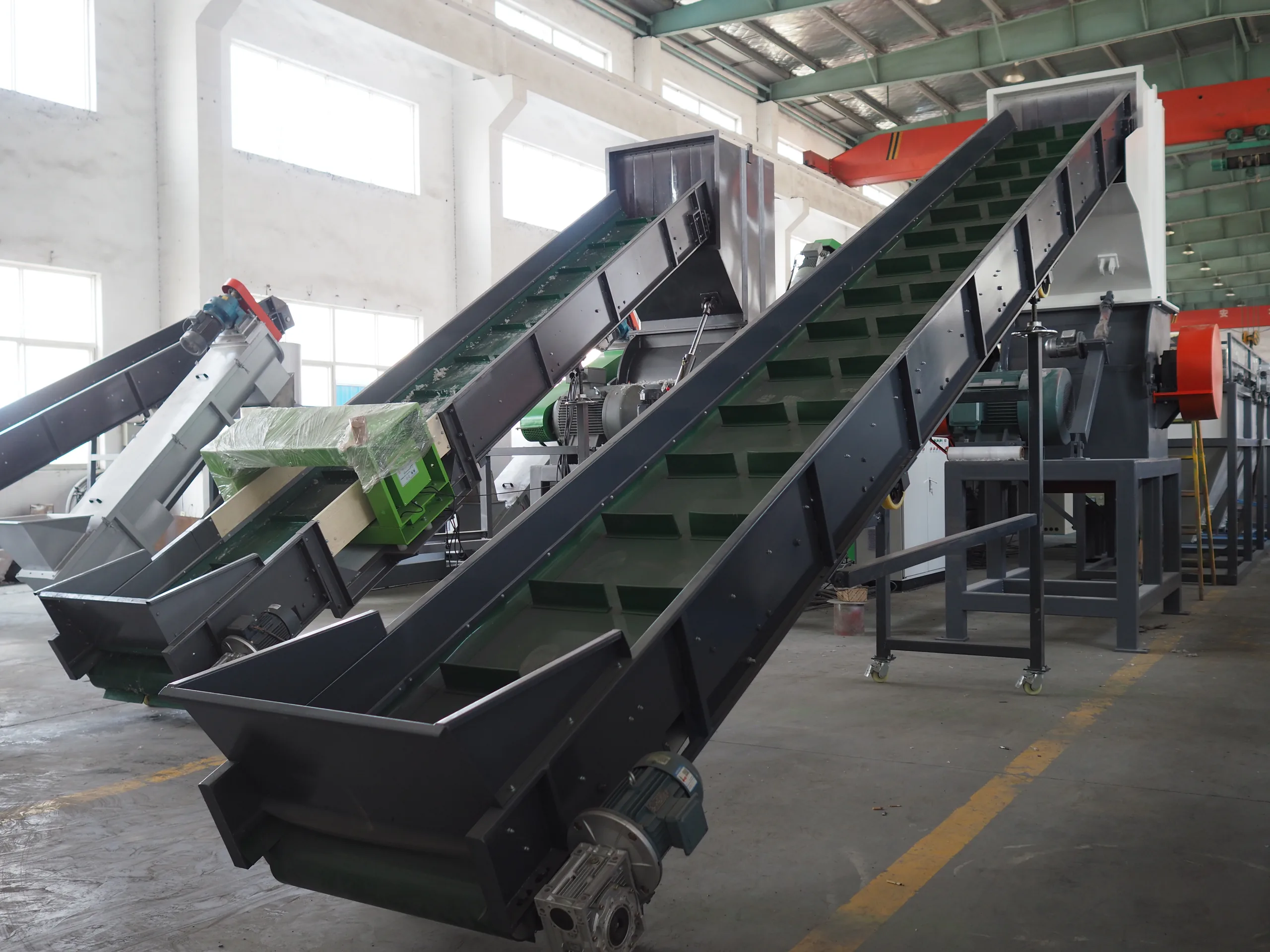 Inclined belt conveyor with tall black side walls on a green steel frame, standing on a workshop floor.