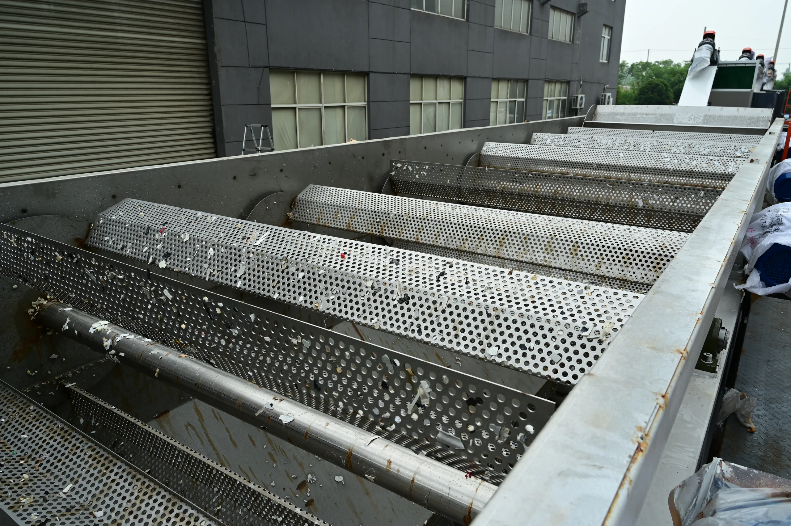Inside of a stainless sink-float washing tank, showing the perforated floor screen and the paddle shafts that walk material along the trough.