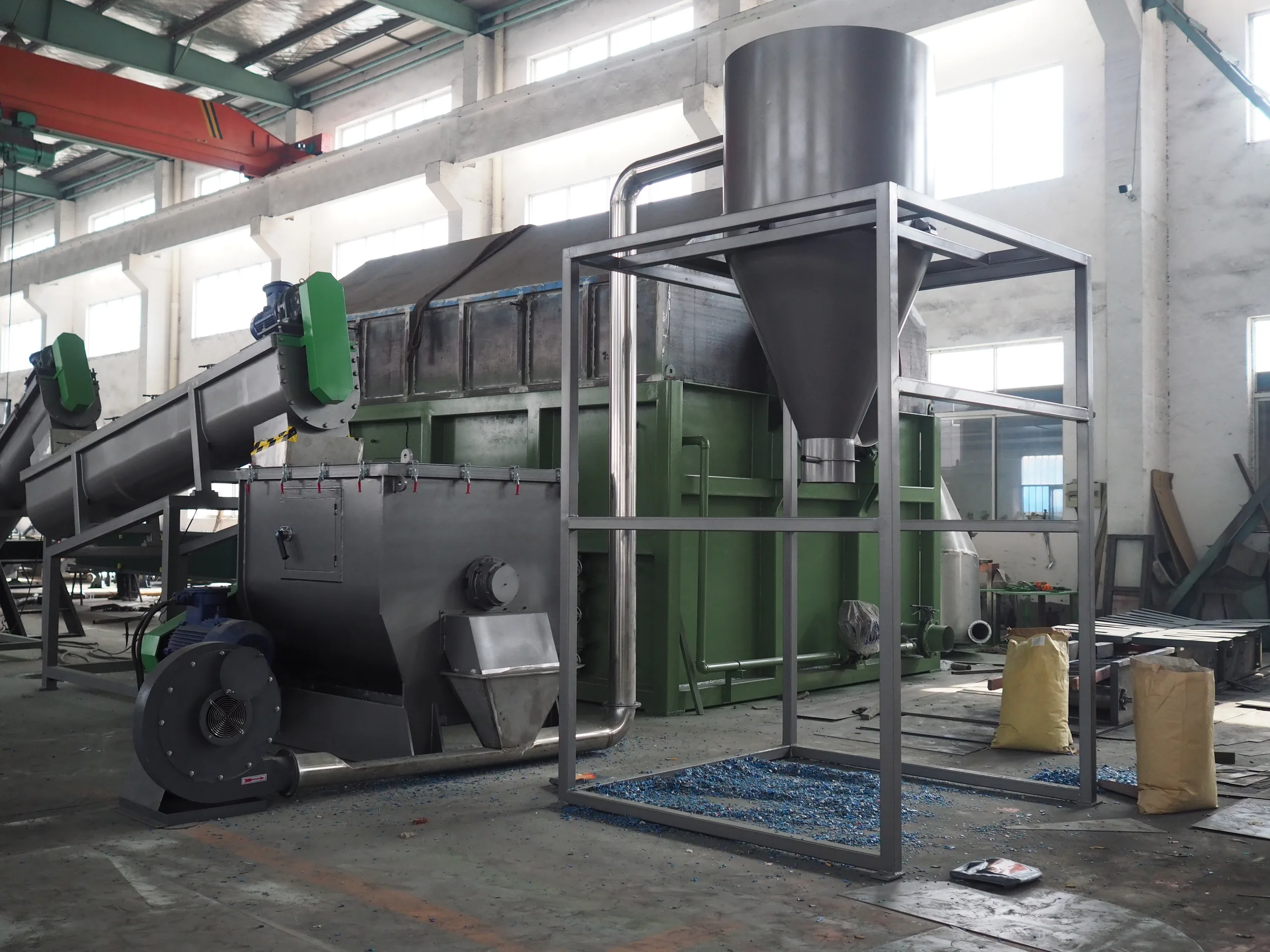 Horizontal stainless storage vessel with green end covers and a cyclone separator mounted above it, joined by ducting inside a workshop.