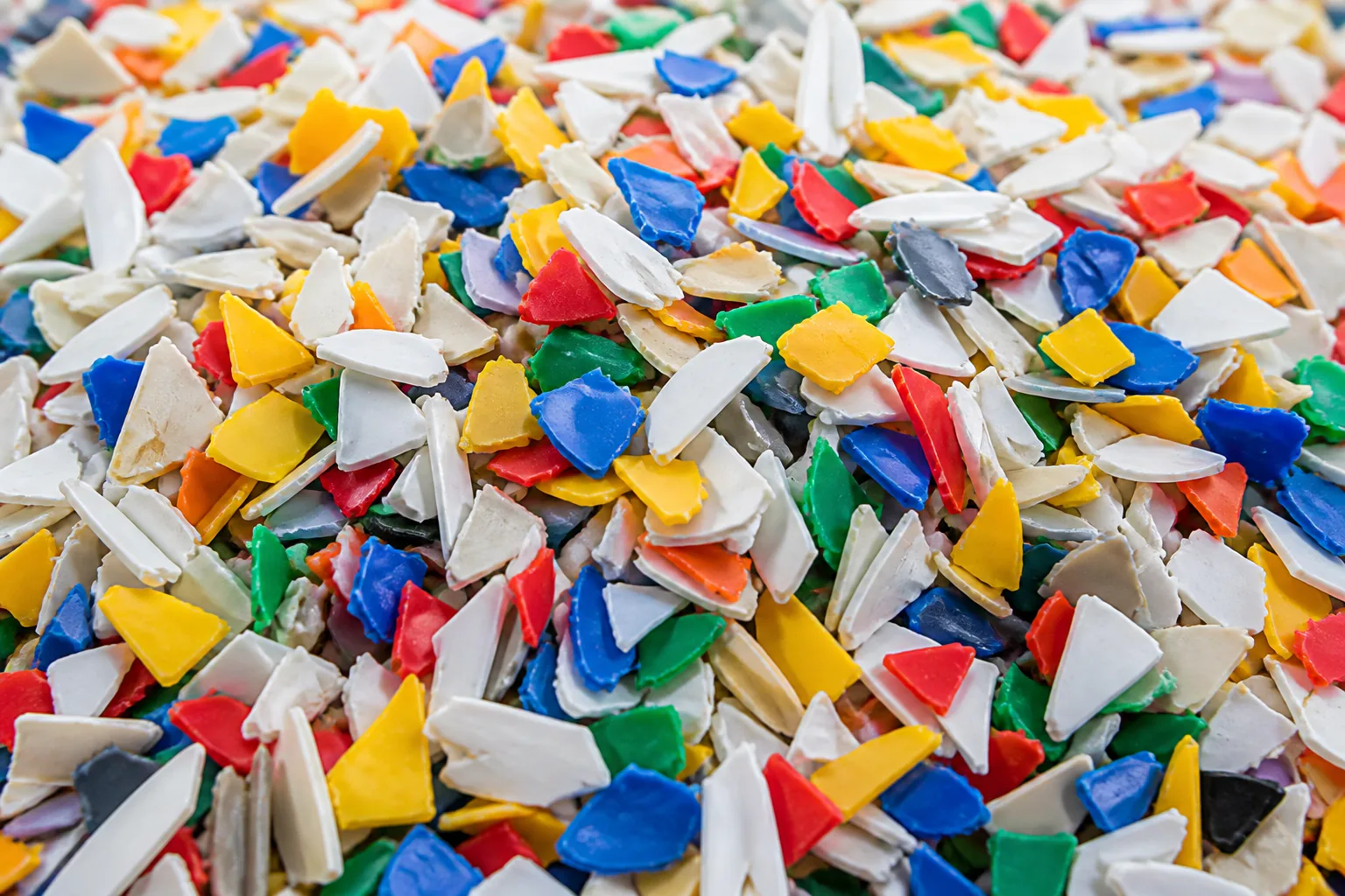 Dense bed of washed mixed-colour rigid regrind, white and cream chips shot through with yellow, red, blue and green pieces.