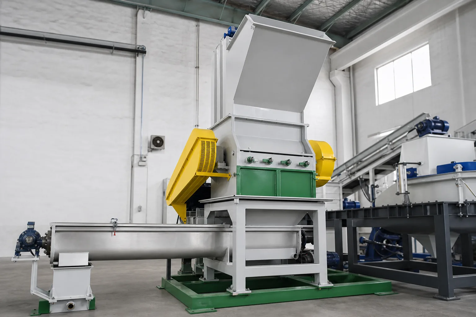 Plastic crusher installed in a washing line workshop with yellow belt guards above a screw conveyor